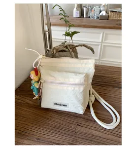 Detail of off-white nylon bucket bag with dual zippers and cute cartoon doll pendant