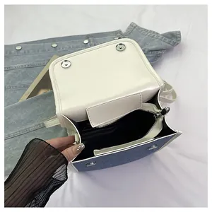 Detail view of denim and white faux leather crossbody bag showing interior and magnetic snaps