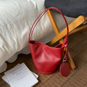 Rote Eimertasche mit Knotendetail am Schultergurt auf rustikalem Holzhintergrund