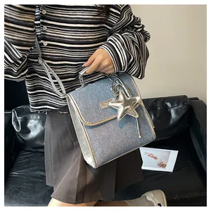 Detail of a denim crossbody bag with silver leather trim and a star charm on a sofa