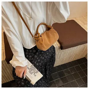 Detail van bruine suède hobo tas met geknoopte handgreep en afneembare schouderriem