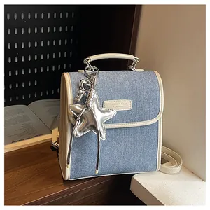 Detail of light blue denim crossbody bag with cream leather trim and star charm on a bookshelf