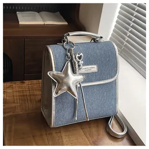 Detail of denim shoulder bag with silver star pendant and metallic logo on dark wood table