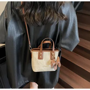 Détail du sac seau en toile et cuir marron avec lettrage doré porté par le mannequin