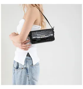 Detail of a black faux leather underarm bag with crocodile texture on a female model