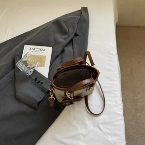 Mini sac seau rétro bicolore avec bordure en cuir sur lin blanc et livre d'art en fond