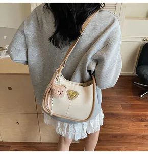 Détail du sac demi-lune crème avec bordure kaki et porte-clés ourson en peluche
