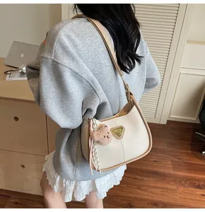 Détail du sac à bandoulière crème avec bordure marron et breloque d'ours en peluche