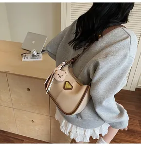 Détail du sac hobo beige avec breloque ours en peluche et triangle sur la bandoulière