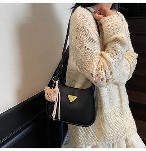 Détail du sac croissant en cuir noir avec logo triangle doré et breloque ours