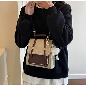 Detail of retro color-block backpack with golden metal buckle and soft plush ball charm