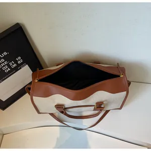 Detail of off-white canvas travel bag featuring brown leather trim and wavy edge design