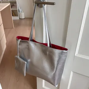Gros plan du sac cabas argenté avec doublure rouge accroché à une porte blanche