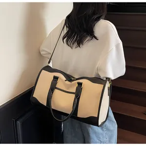 Rear view of a model carrying a beige canvas travel bag with black leather trim on a staircase
