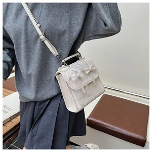 Dettaglio di una borsa a tracolla vintage bianco crema con catena di perle e fiocco