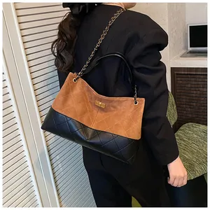 Détail d'un sac seau en daim marron et cuir matelassé noir porté à l'épaule