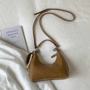 Detail of a brown woven underarm bag featuring a beaded charm on a soft fabric background
