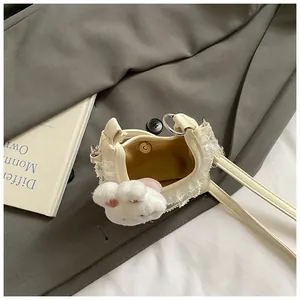 Detail der cremefarbenen Mini-Cloud-Tasche mit Spitzenbesatz und Plüsch-Hasen-Anhänger