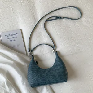 Detail of blue woven texture handbag with silver hardware and adjustable strap on white fabric
