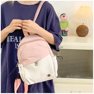Close-up of pink and white mini backpack showing front zipper pocket and metal logo detail
