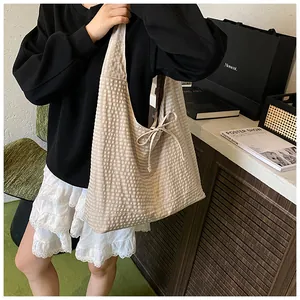 Close-up of beige textured tote bag with elegant side bow detail and plaid fabric texture