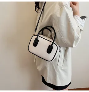 Detail of white bowling bag with black trim worn as a crossbody by a model on plain background