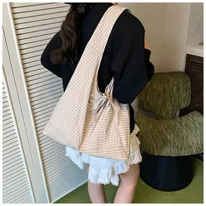 Macro detail of checkered canvas tote bag with side ribbon bow on model's shoulder