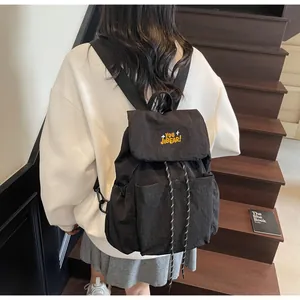 Vista laterale di uno zaino in nylon nero con ricamo giallo indossato da una modella