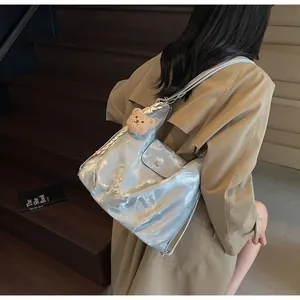Silver metallic shoulder bag with chain strap and teddy bear charm on model in scene
