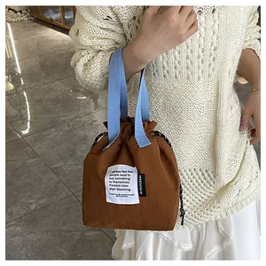 Detalle de bolsa de almuerzo con cordón, tela marrón, asas azules y etiqueta artística
