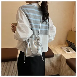 Silver bucket bag with chain handle shown on model in a stylish indoor setting