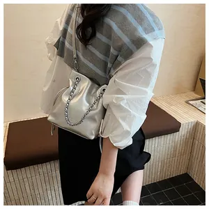 Chic silver bucket bag with metal chain detail shown on a model in a minimalist setting