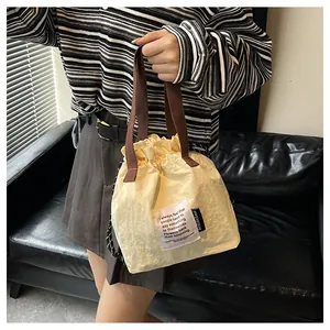 Detalle de la bolsa de almuerzo crema con cordón, asas marrones y parche impreso