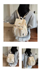 Dettaglio dello zaino in nylon crema con chiusura a coulisse e scritte ricamate gialle