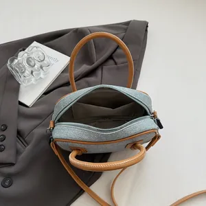 Mini denim bowling bag with camel leather straps shown from a top-down aesthetic angle
