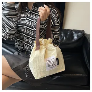 Detalle de bolsa de almuerzo crema con cordón, asas marrones y forro de rayas