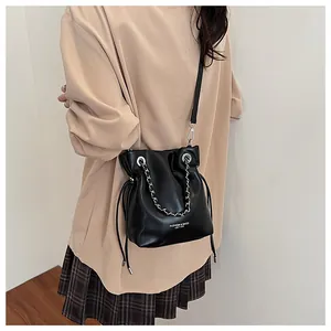 Detail of black leather bucket bag with chain handle and adjustable crossbody strap