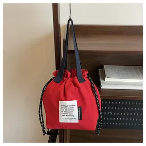 Detalle de bolsa de almuerzo roja con cordón y asa azul sobre estante de madera