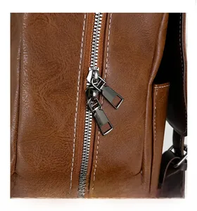 Close-up of smooth gray metal zippers and white stitching on brown leather business bag