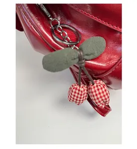Close-up of red glossy leather bag featuring a cute cherry charm with plaid fabric detail