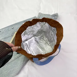 Bolsa de almuerzo aislada de lona marrón con asas azules e interior de papel térmico