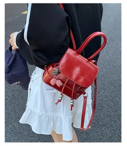 Detail of red faux leather mini backpack with drawstring, cherry charm and top handle