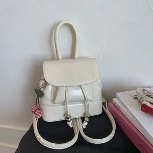 Detail of cream vintage backpack with drawstrings and red cherry charm accessory