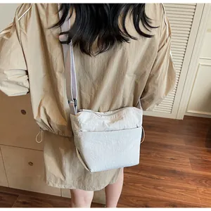 Detail showing the adjustable wide nylon shoulder strap and beige fabric of the crossbody bag
