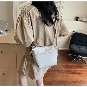 Detailed view of grey pleated crossbody bag shown on model in cozy home setting