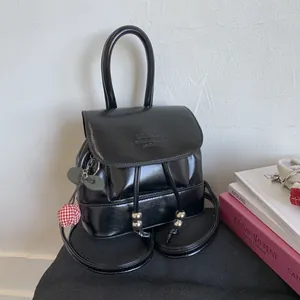 Detail of glossy black mini backpack featuring a cherry pendant and metallic drawstring beads