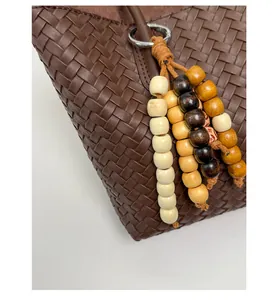Detail of dark brown woven leather tote with multi-color wooden bead charm and metal ring