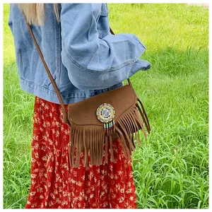 Sac bandoulière bohème marron à franges porté avec une robe à fleurs sur l'herbe