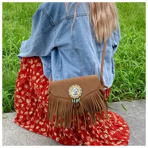 Détail d'un sac bohème à franges marron avec badge brodé de perles colorées et pompons longs