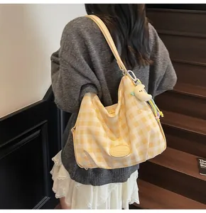 Détail du sac fourre-tout à carreaux jaunes avec étiquette en cuir et breloque lune en peluche